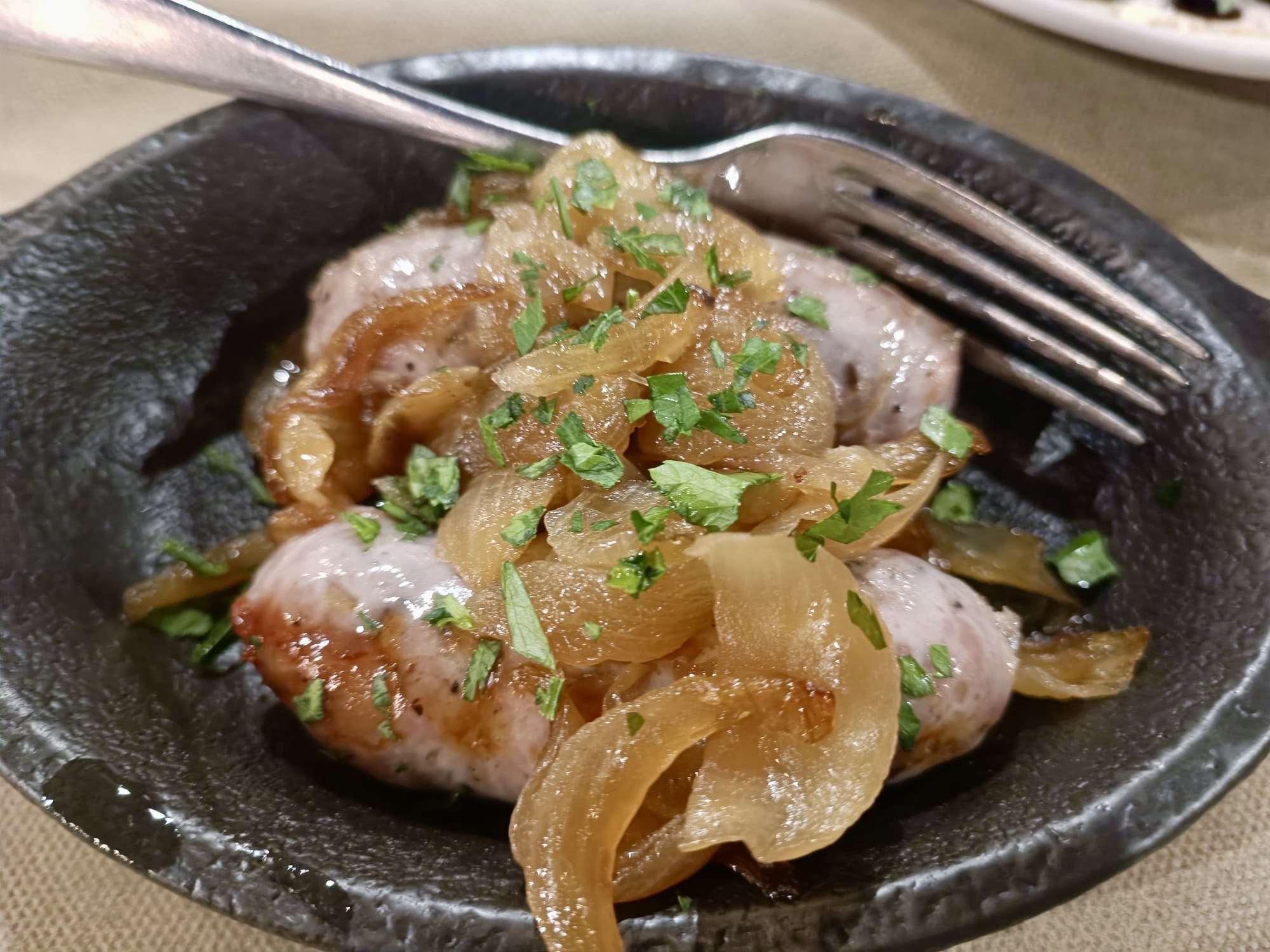 Salsiccia con cipollata siciliana servita calda con cipolle caramellate e prezzemolo fresco